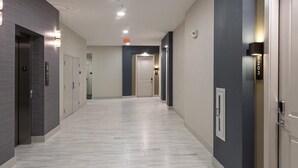 Een hotelgangen met een lichtgekleurde betegelde vloer, een moderne lift en een deur met nummerbord.