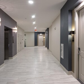 A hotel corridor with a light-colored tiled floor, a modern elevator, and a door with a number sign. - Landing | Stylish 2BD, Gym (Houston)