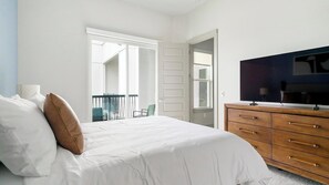 A bedroom with a bed, a dresser, a television, and a balcony. - Landing | Stunning 2BD, Gym (Houston)