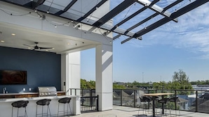 Eine Terrasse im Freien mit Barbereich, Sitzgelegenheiten und Blick auf die Stadtlandschaft.