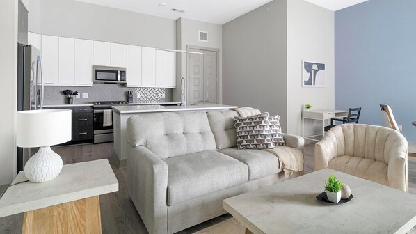 A modern living room with a sofa, armchair, coffee table, and a small side table with a lamp. - Landing | Stunning 2BD, Gym (Houston)