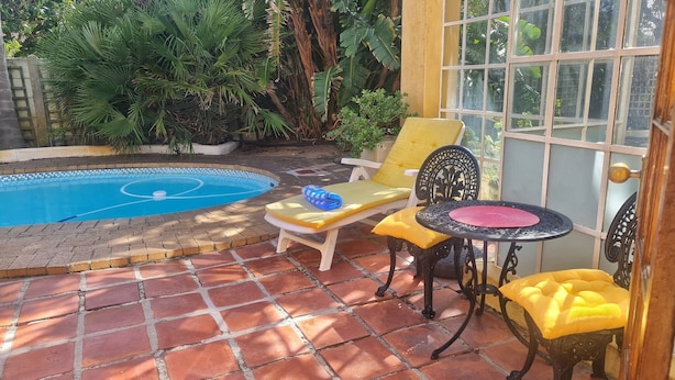 Zona de piscina amb paviment de rajola, una piscina i mobiliari exterior, incloent una cadira i taula.