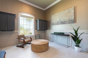 A spacious room with a large window, dark cabinets, a woven ottoman, a console table, and a potted plant. - Landing | Beautiful 2BD, Clubhouse, Gym (Cocoa)