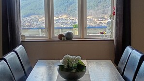 A dining area with a table, chairs, a bowl of flowers, and a view through large windows.