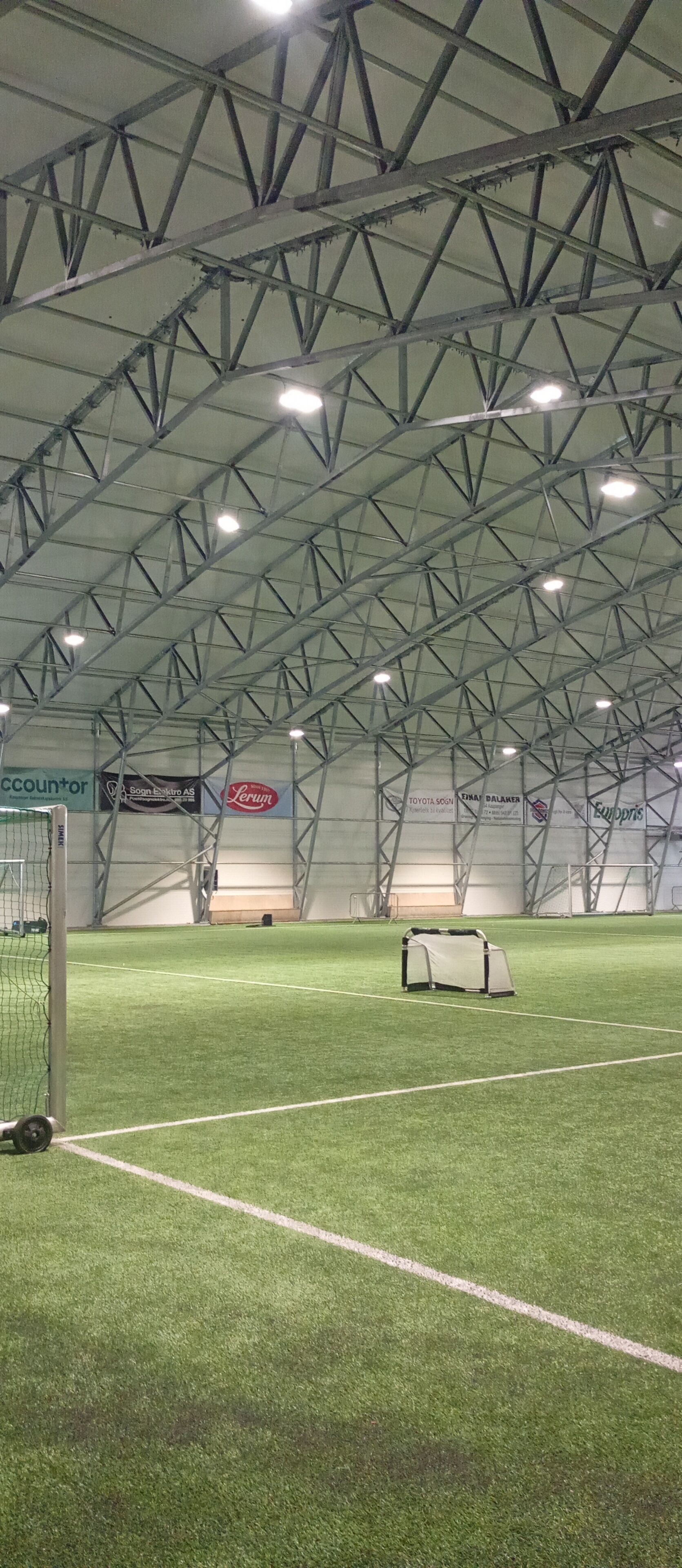 An indoor sports facility with artificial turf, goalposts, and a covered seating area.