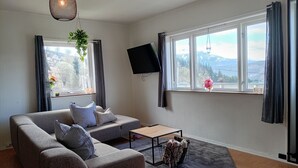 A living room with a sofa, a coffee table, a TV, and a window with a view of mountains.