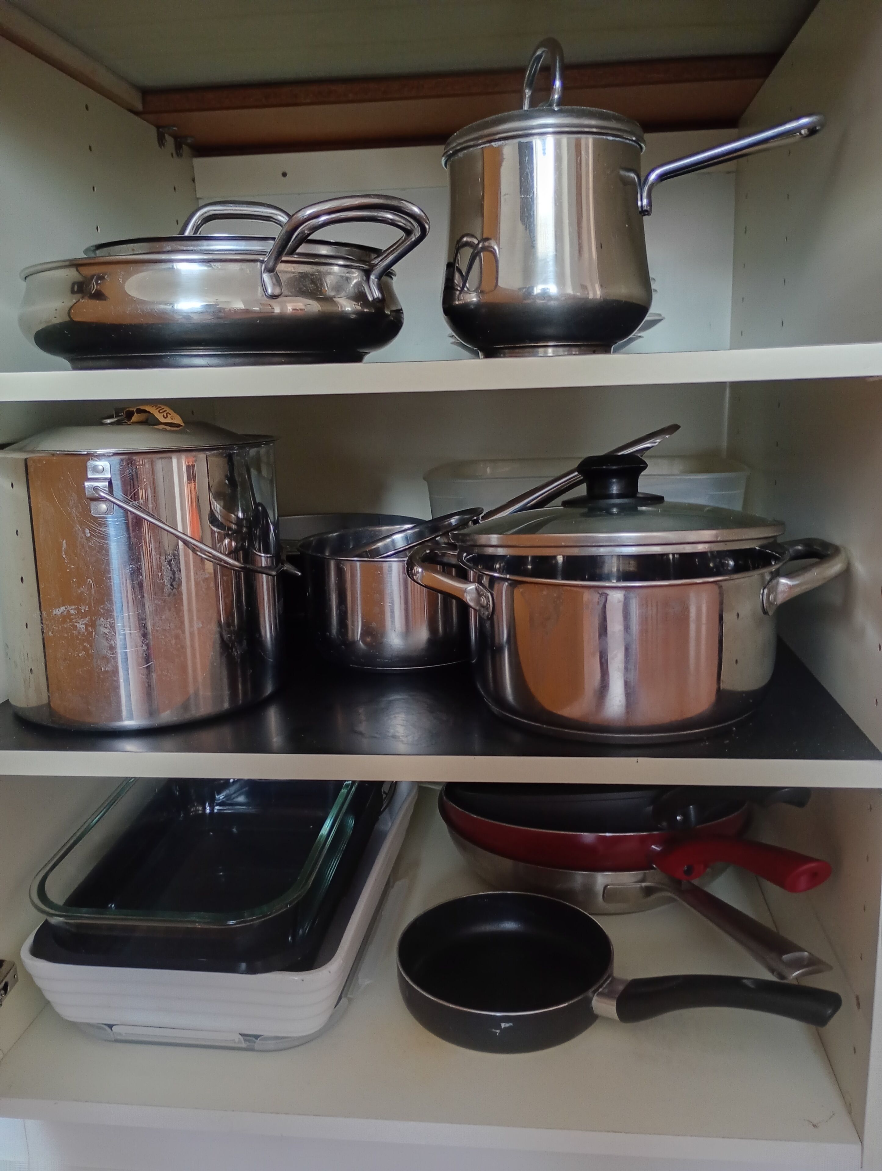 Un estante de cocina con utensilios de acero inoxidable, incluyendo ollas, sartenes y una fuente para hornear.