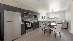 Een moderne keuken met een koelkast, fornuis, magnetron en een eethoek met stoelen en een tafel.