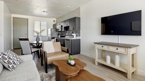 Een modern appartement met een woonef, eetgedeelte, kitchenette en een aan de muur bevestigde televisie.