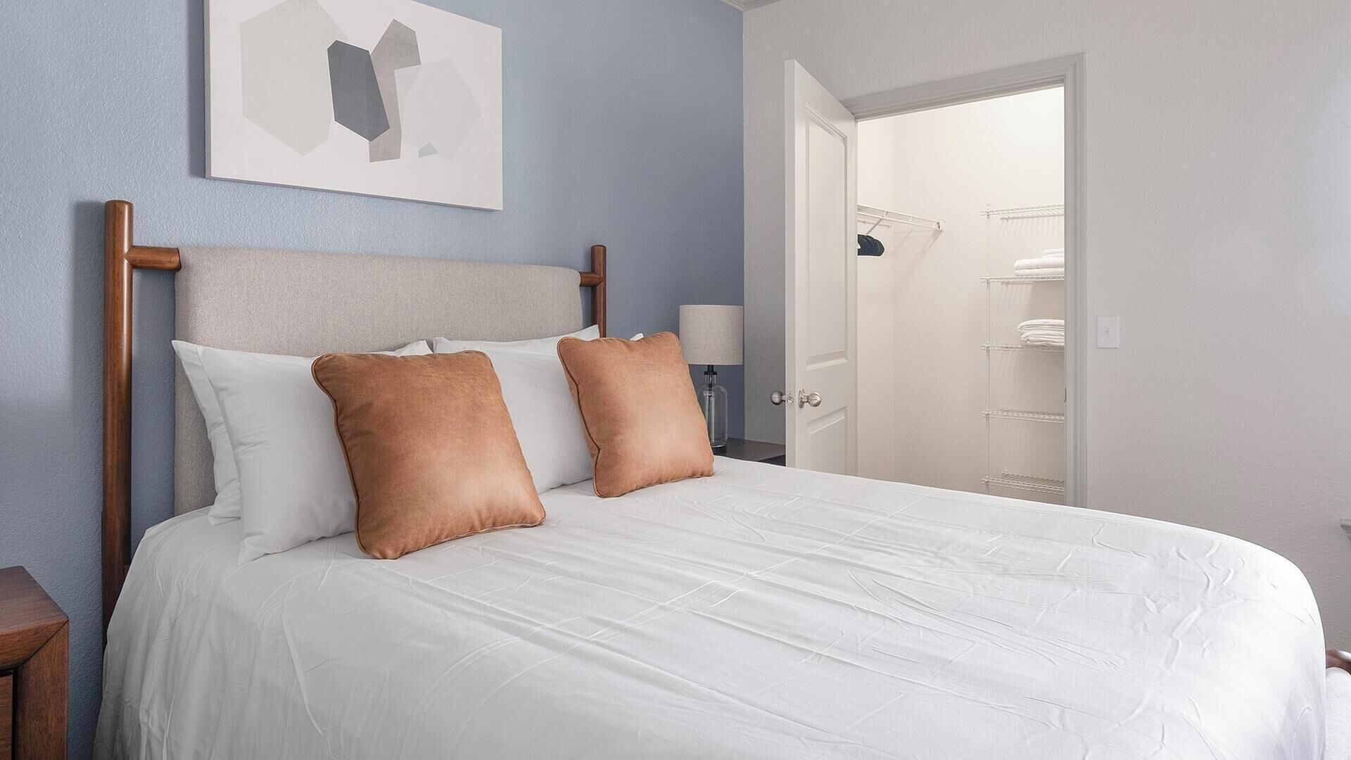 Una habitación de hotel con cama, mesita de noche, lámpara y puerta que da a un baño.