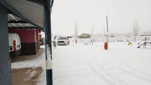 A snowy outdoor area with a covered building, a parked car, and a playground. - Cabañas Los Nogales: Mountain Cabin N°1 (Uspallata)