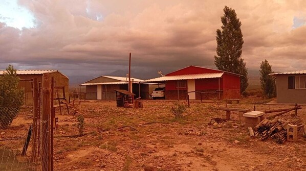 A rural setting with a dirt ground, a few buildings, and a cloudy sky.