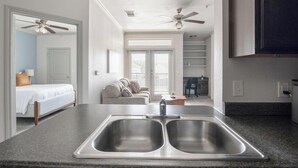 Een moderne keuken met een dubbele spoelbak, een zithoek met een bank, en een slaapkamer met een bed en een plafondventilator.