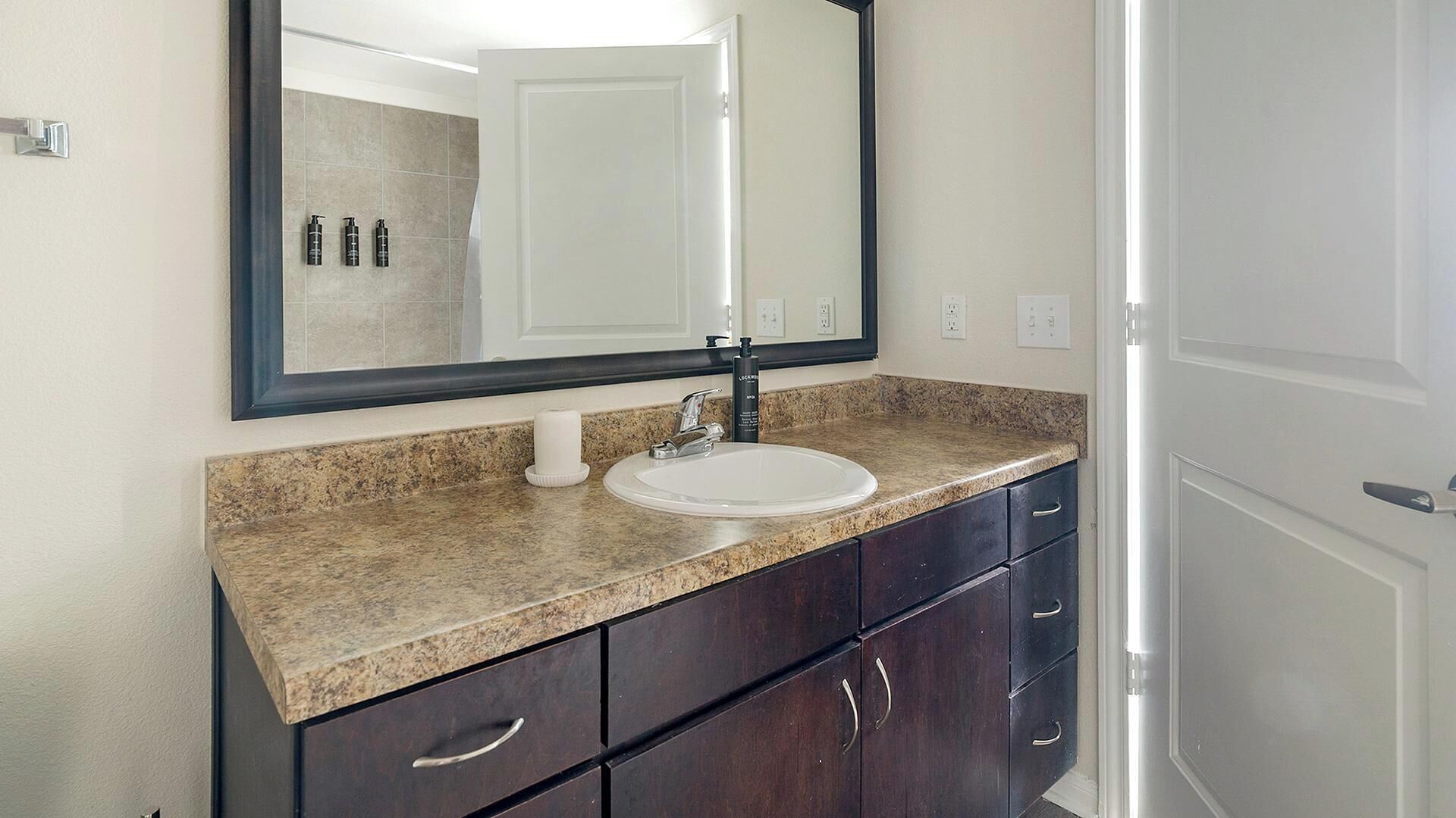 A bathroom with a white sink, dark wooden cabinets, a granite countertop, and a large mirror.