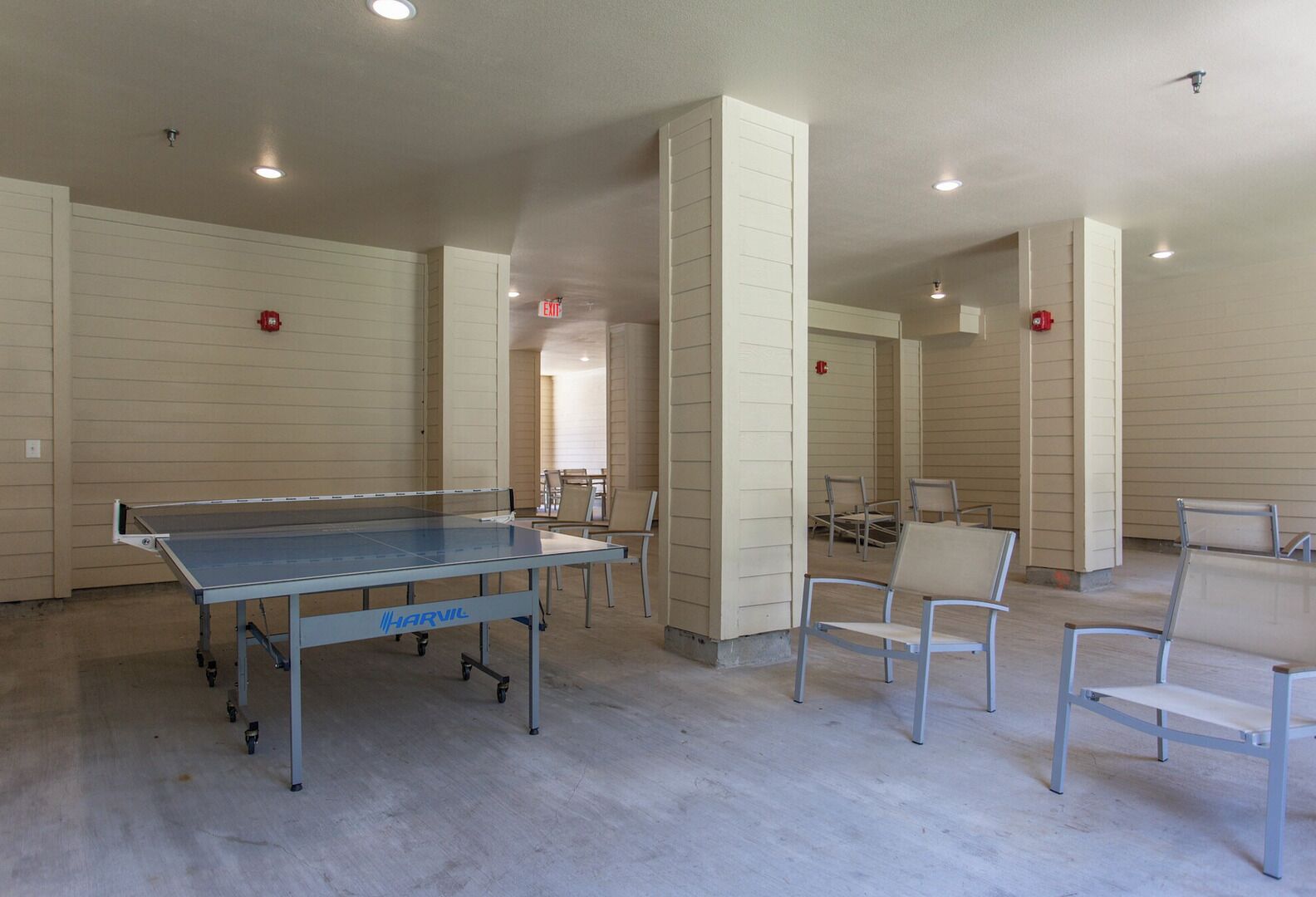 Un'ampia area interna con un tavolo da ping pong, diversi posti a sedere e un cartello di uscita ben visibile.