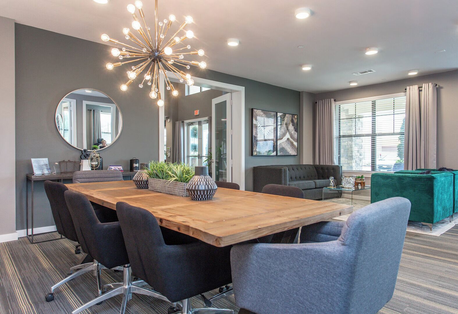 A conference room with a wooden table, black chairs, a modern chandelier, a sofa, and a TV.