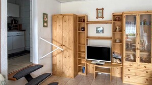 Ein gemütlicher Wohnraum mit Fernseher, Holzmöbeln und Küchenzeile.
