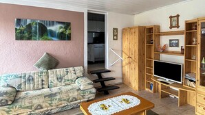 Ein Wohnzimmer mit einer Couch, einem Fernseher, Holzbögen und einem Gemälde.