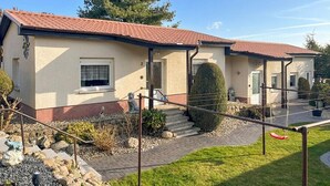Ein zweigeschossiges Haus mit rotem Ziegeldach, einer Veranda und einem Kiesweg zum Eingang.