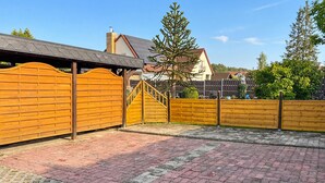 Eine gepflasterte Terrasse mit Holzlattenzaun, einer Metalltreppe und einem Baum im Hintergrund.