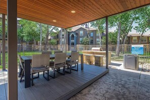 An outdoor patio with wicker furniture, a grill, and a stone barbecue area. - Landing | Stylish 2BD in Cityview (Fort Worth)