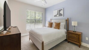 A bedroom with a bed, bedside table, lamp, and a TV on a stand. - Landing | Stylish 2BD in Cityview (Fort Worth)