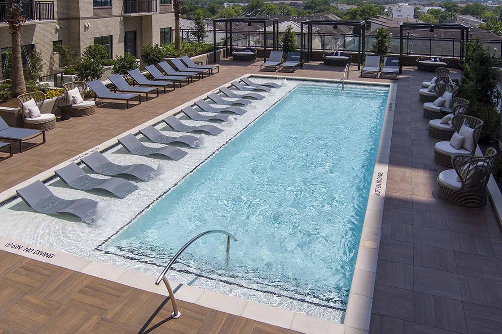 A rooftop pool with lounge chairs and a glass balustrade.