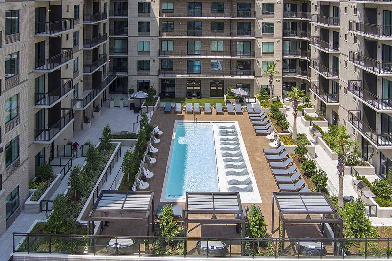 A rooftop pool with sun loungers and a view of high-rise buildings.