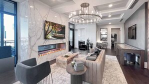 A modern living room with a fireplace, a large TV, and a chandelier. - Landing | Stylish Studio, Gym, Clubhouse (Houston)