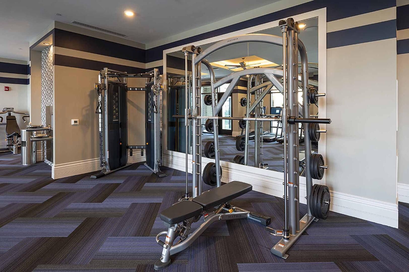 A gym with weightlifting equipment, a bench, and a mirror.