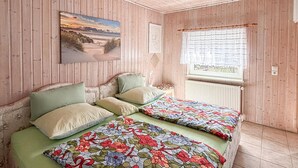 Una habitación con paneles de madera, dos camas con ropa de cama floral, un cuadro de una playa y una ventana con vistas.