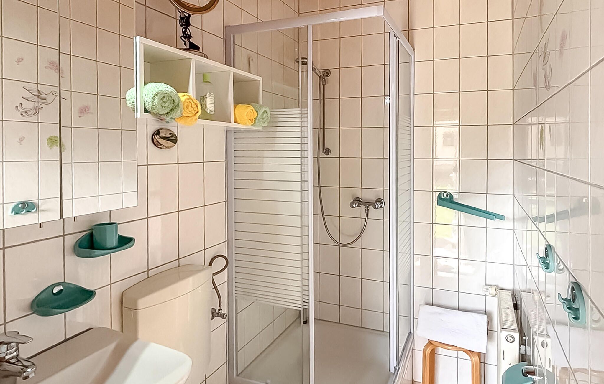 Een badkamer met douche, toilet, wastafel en spiegel met een plank erboven.