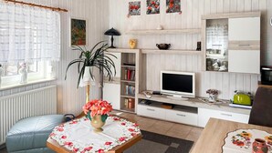 Una sala de estar con televisor, estantería y una planta.