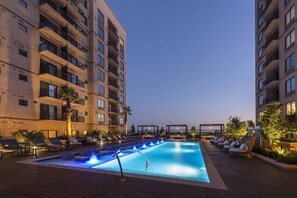 A rooftop pool with lounge chairs and a water feature, surrounded by high-rise buildings. - Landing | Stylish Studio, Gym, Yoga Studio (Houston)