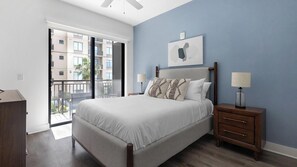 A bedroom with a bed, nightstands, a lamp, a picture on the wall, and a balcony with a view of buildings. - Landing | Stylish Studio, Gym, Yoga Studio (Houston)