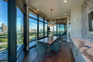 A modern dining area with a long table, chairs, and a city view through large windows. - Landing | Stylish Studio, Gym, Yoga Studio (Houston)