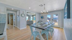 A dining area with a long table, light blue chairs, and a chandelier. - Barefoot and Salty & Tequila Tides by Avantstay. Sleeps 20 2 Homes + Dual Pools + Golf Cart 5 Min to Beach Port Aransas (Port Aransas)