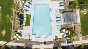 Vista aérea de una zona de piscina con múltiples sillas de descanso, sombrillas y una zona de estar cubierta.