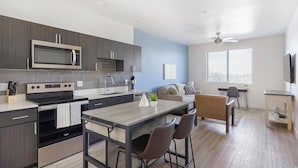 Una cocina moderna con microondas, estufa y lavaplatos, un comedor con mesa y sillas, un sofá y un ventilador de techo.