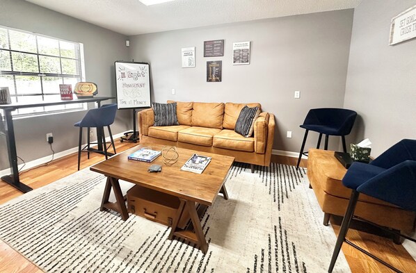 A living room with a brown leather sofa, a wooden coffee table, a blue chair, and a whiteboard on the wall.