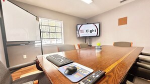 Ett konferensrum med ett träbord, stolar, en tv-skärm, ett tangentbord, en mus och en fjärrkontroll.