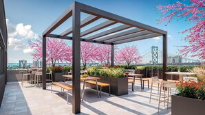 Een terras op het dak met een pergola, zitplaatsen en kersenbloesems.