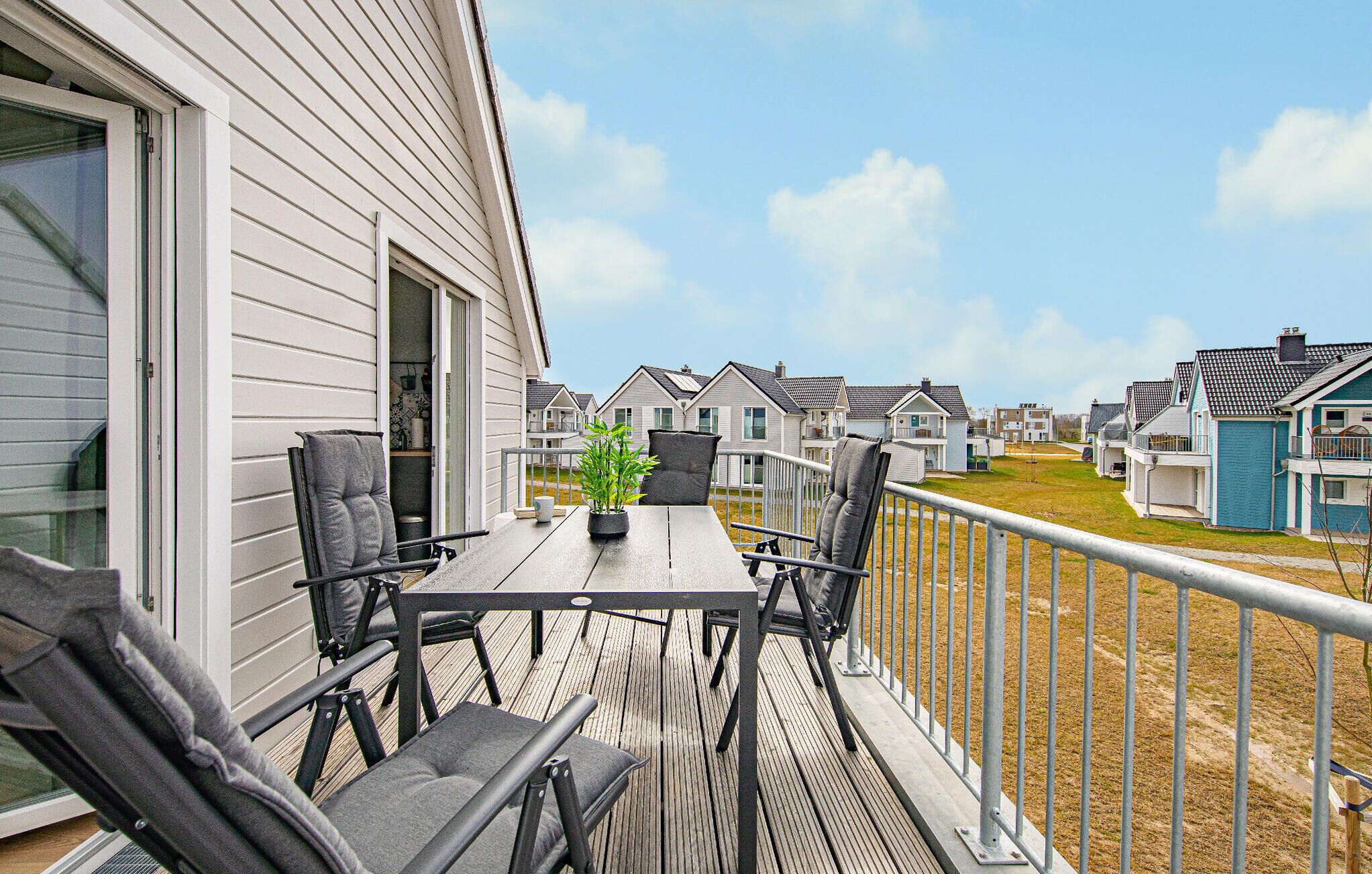 A balcony with a table and chairs, overlooking a row of similar houses.