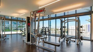 Ein Fitnessstudio mit Gewichthebern, Bänken und Blick auf Gebäude durch große Fenster.