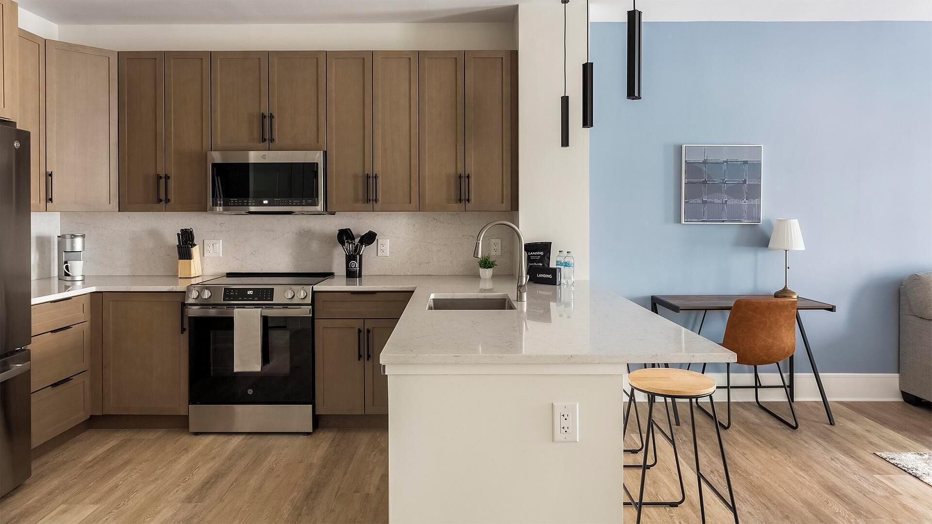 A modern kitchen with wooden cabinets, stainless steel appliances, a marble countertop, and a bar area with stools.