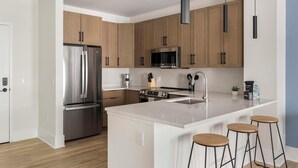 Eine moderne Küche mit Edelstahlgeräten, Holzschränken und einer zentralen Kochinsel mit Barhocker.