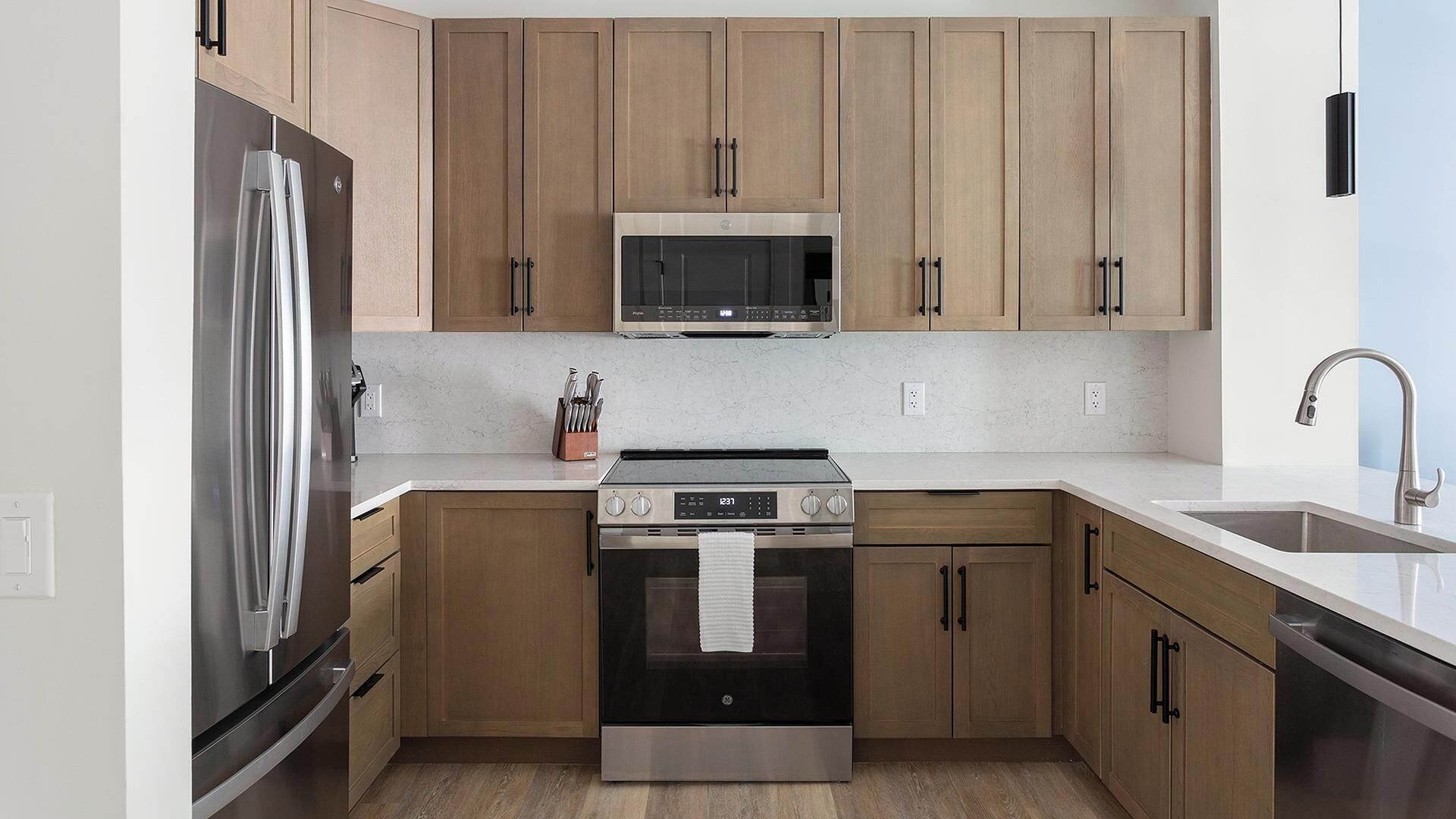 A modern kitchen with stainless steel appliances, wooden cabinets, and a white countertop.