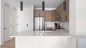 Une cuisine moderne dotée d’un réfrigérateur en acier inoxydable, de meubles en bois et de luminaires suspendus.