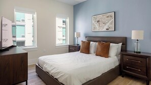 Une chambre à coucher avec un lit, des tables de chevet, un bureau et une fenêtre.