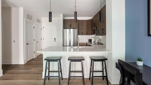 A modern kitchen with a central island, stainless steel appliances, and pendant lighting. - Landing | Chic 1BD, Pool (Philadelphia)
